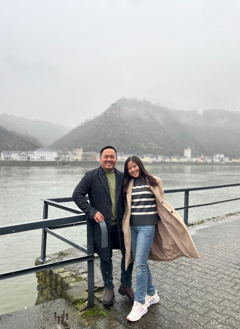 Two people posing in front of a river and hillside.