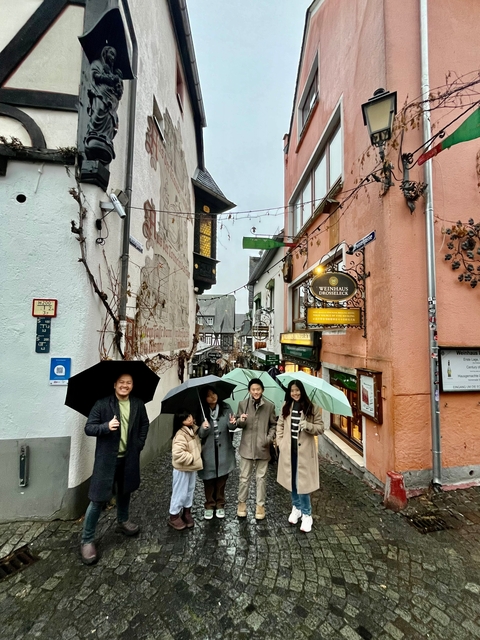 A group with umbrellas in a quaint, narrow street with shops.