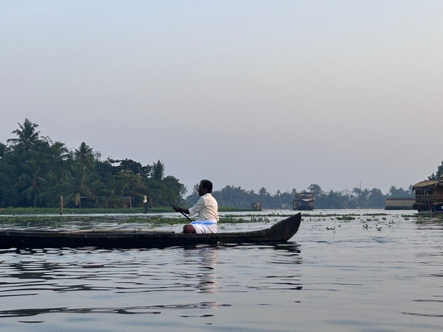       Man paddling a canoe on a calm river with palm trees.
  