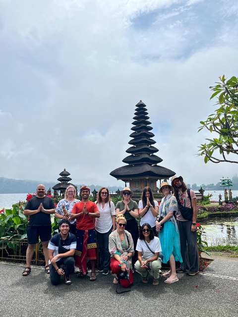 Group smiling in front of a lakeside temple, cloudy skies.