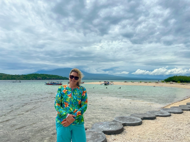 Woman standing on a sandy beach with ocean and mountain view.