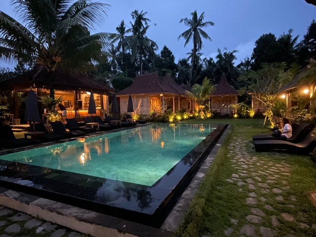 Pool area with traditional bungalows and lush greenery at night.