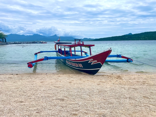 Traditional boat on a sandy beach with mountains in the background.