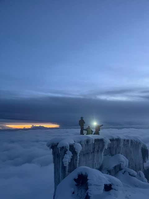 Silhouettes on a cloud-covered ridge at sunset.