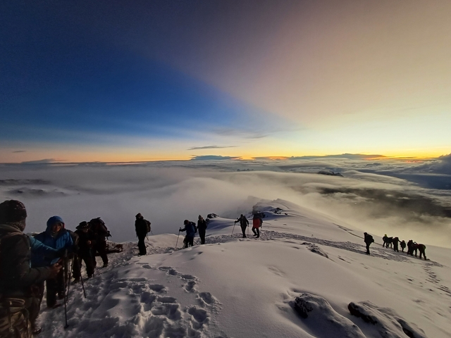 Hikers making their way across a snowy mountain ridge at dawn.