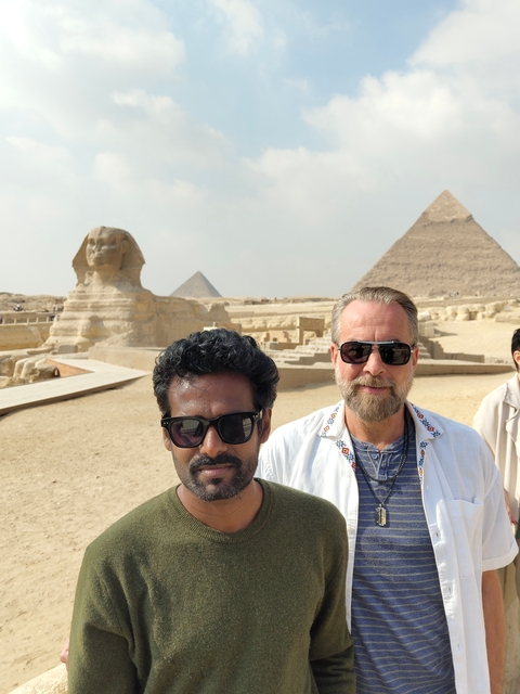 Two men taking a selfie with the Sphinx and pyramids in the background.