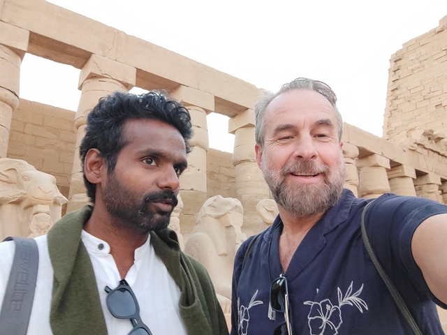       Two men taking a selfie in front of ancient statues in Egypt.
  