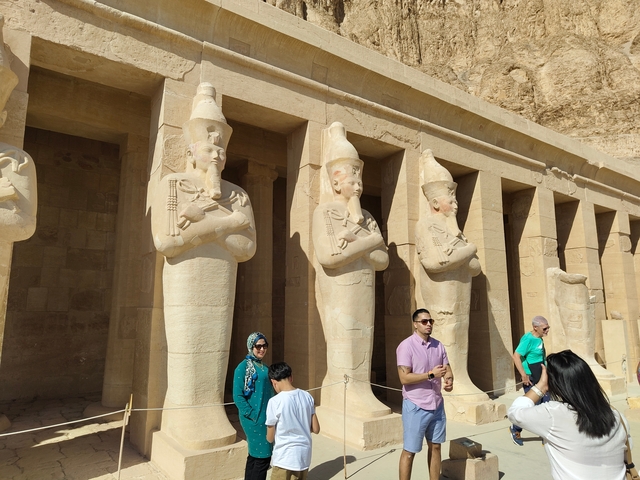       Visitors wandering through an ancient Egyptian temple with statues.
  