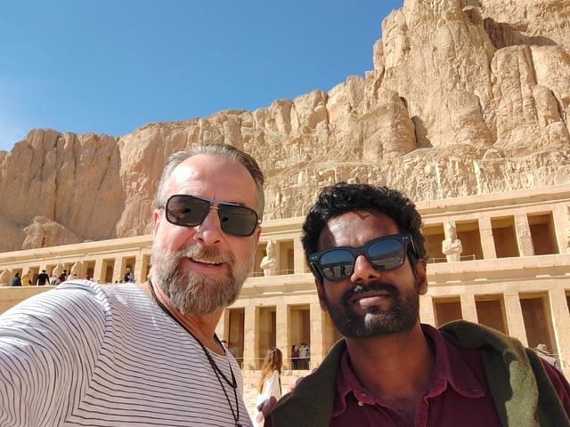       Two men standing in front of an ancient temple carved into the mountainside.
  
