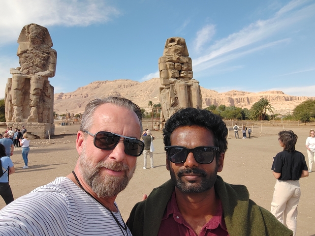Two men taking a selfie with the massive statues of Memnon in the background.