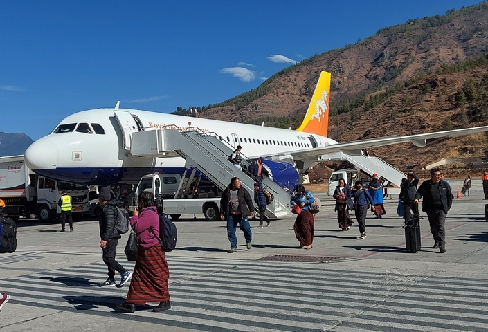 Passengers disembarking from a plane at an airport with mountainous background.