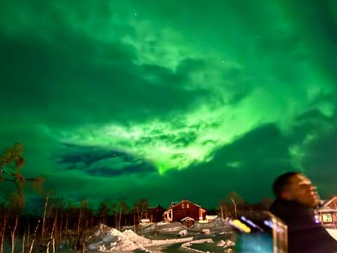 Northern lights in the sky with a person and a house below.