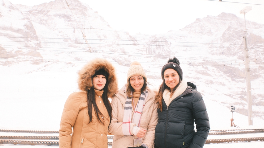 Three women posing in winter attire with snowy mountains behind.
