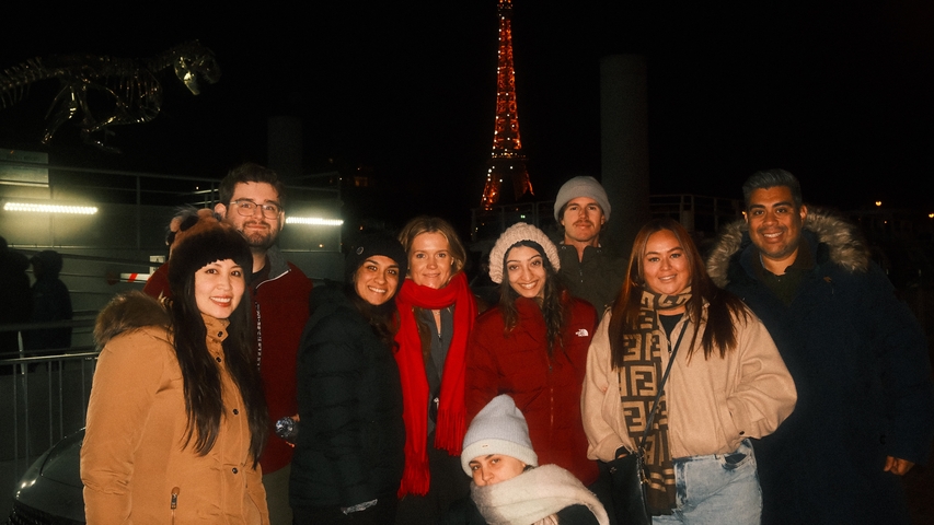 Group of people in winter clothing posing at night with a landmark.