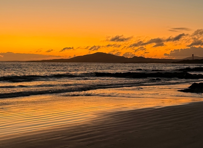 Beautiful sunset over a beach with a lighthouse and ocean waves.