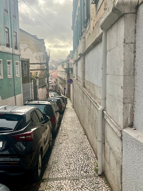       A narrow street with parked cars in an urban setting.
  