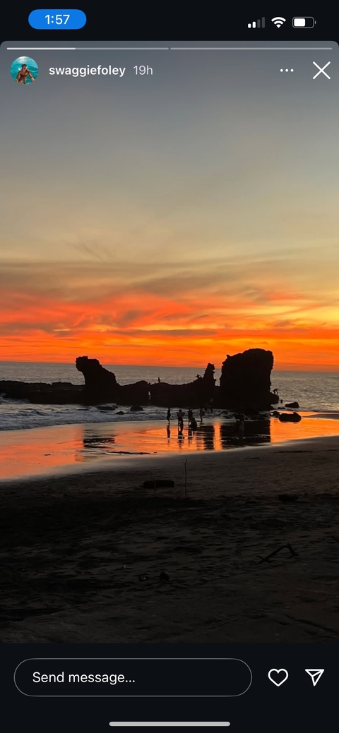 A beach during sunset with silhouettes of people and rocks.