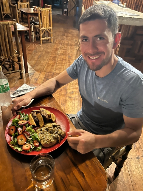       Smiling person enjoying a meal at a wooden table.
  