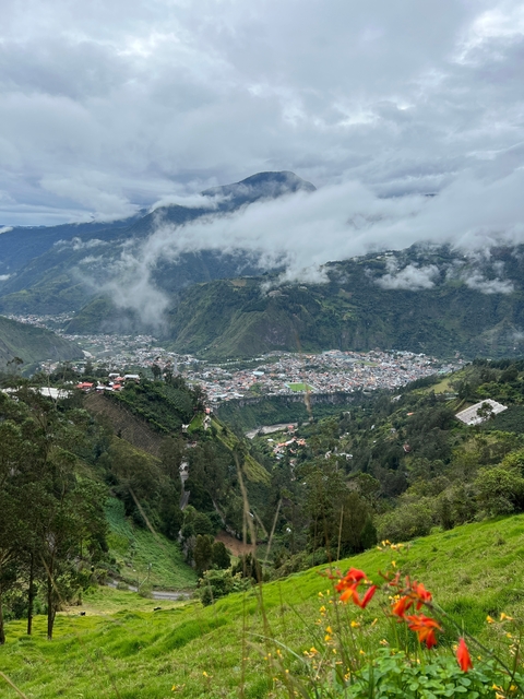      Expansive view of a town situated in a green mountainous valley with clouds.
  