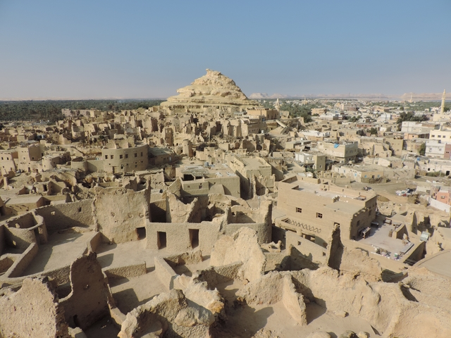 Ruins of an ancient fortress with a pyramid-shaped hill in the background.