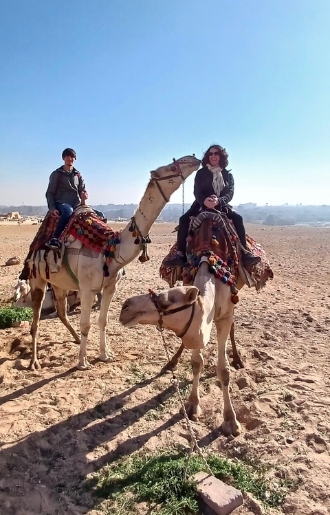       Two people riding camels in a desert landscape.
  