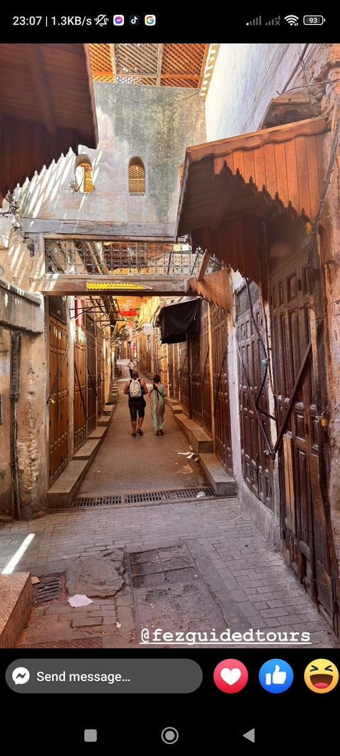       Two people walking through a narrow alleyway in a traditional Moroccan market.
  