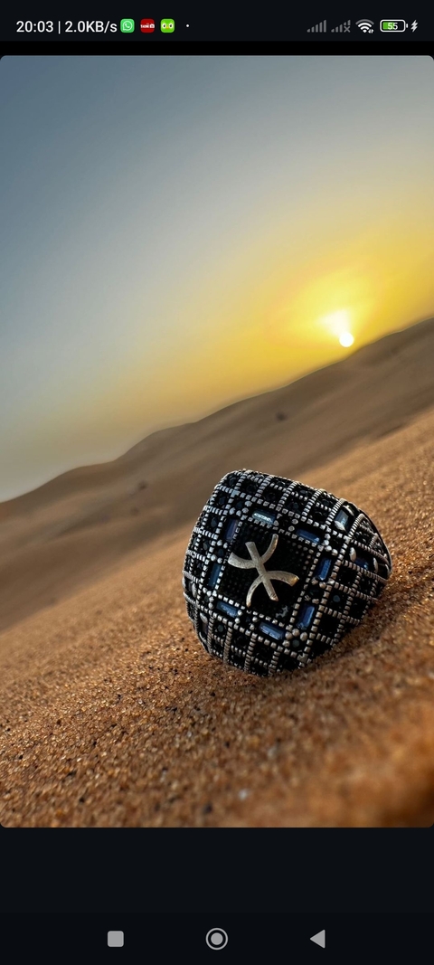       A ring with a Berber symbol resting on sand dunes during sunset.
  