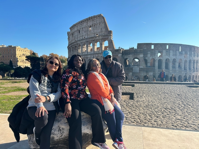 A group of people posing in front of the Colosseum on a sunny day.