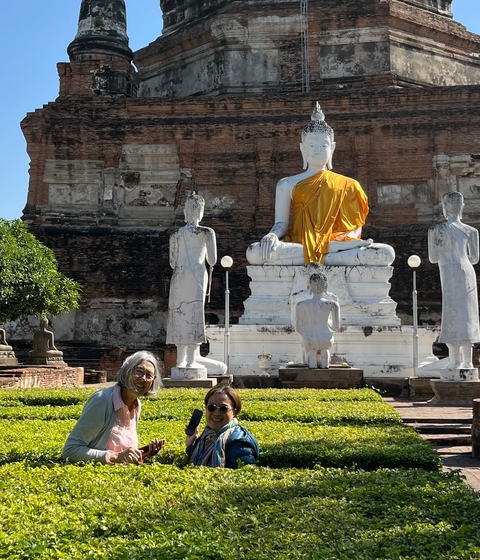 Two people posing near a large Buddha statue with smaller statues.