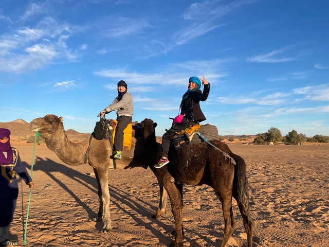       Two people riding camels in a desert landscape.
  