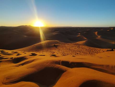 Sunset over sand dunes in a desert landscape.