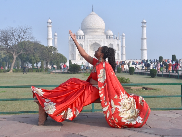 Woman in a red sari posing with the Taj Mahal.