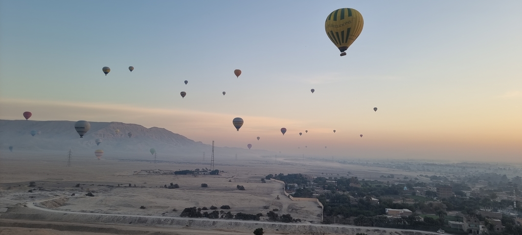 Multiple hot air balloons flying over a desert landscape at sunrise.
