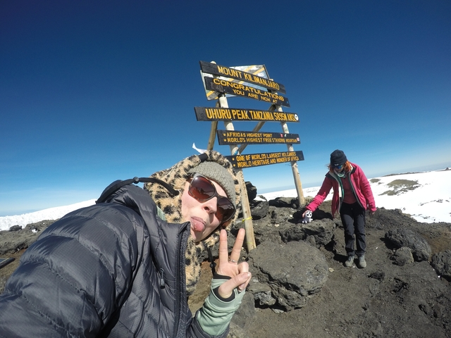 Individuals at Uhuru Peak with sign and snow-capped mountains.