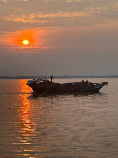 Boat on water with orange sunset reflecting.