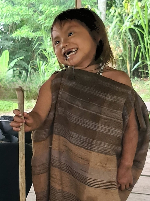       Child dressed in traditional clothing with a wooden stick.
  