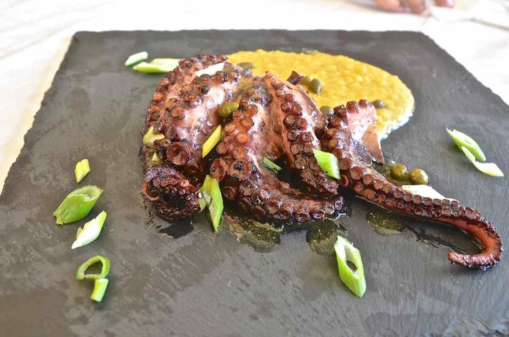 Close-up of a gourmet octopus dish with garnish on a slate platter.