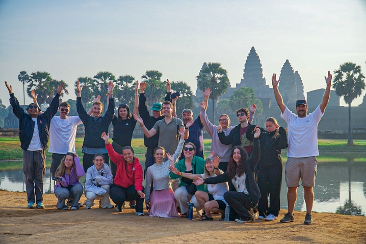       Large group of people posing with ancient temple structures behind.
  