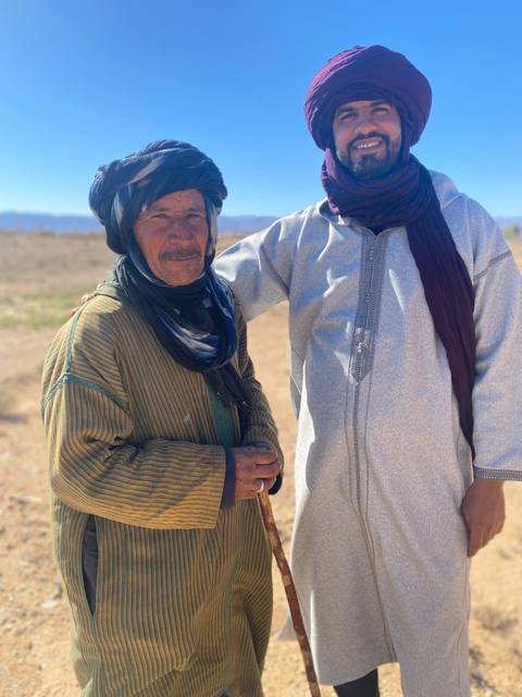 Two people posing in traditional clothing in a rural setting.