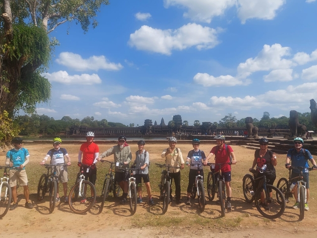Group of cyclists in front of ancient temple ruins.