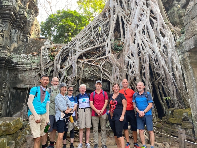 Group of tourists standing at temple ruins engulfed by tree roots.