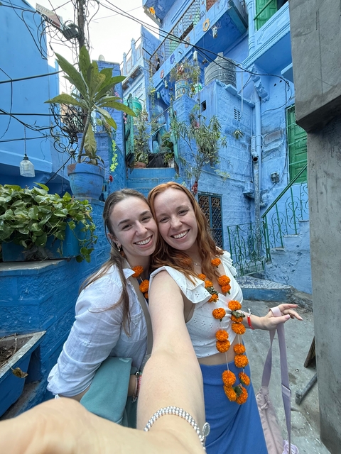 Two people smiling and posing in front of blue-painted buildings.