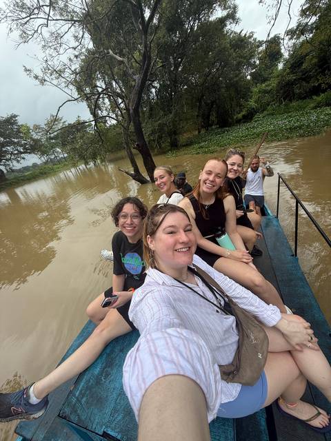 People in a boat tour on a river surrounded by greenery.