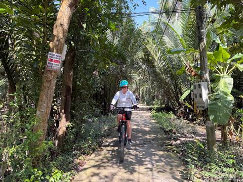 A person cycling on a narrow path surrounded by lush tropical vegetation.