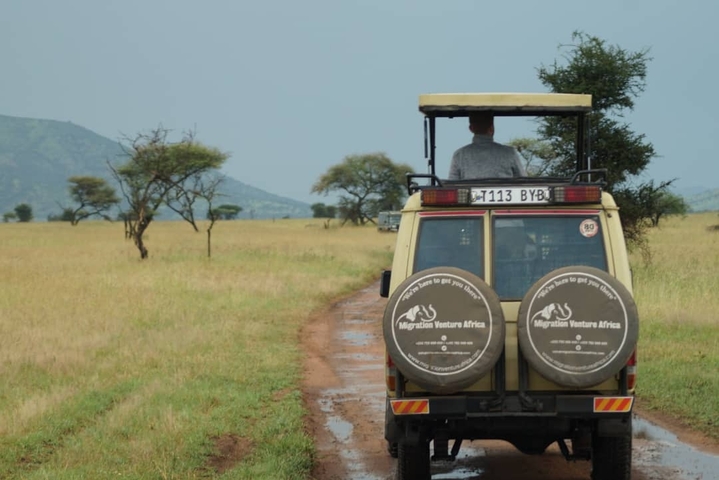       Safari vehicle driving through the savannah with a distant mountain.
  