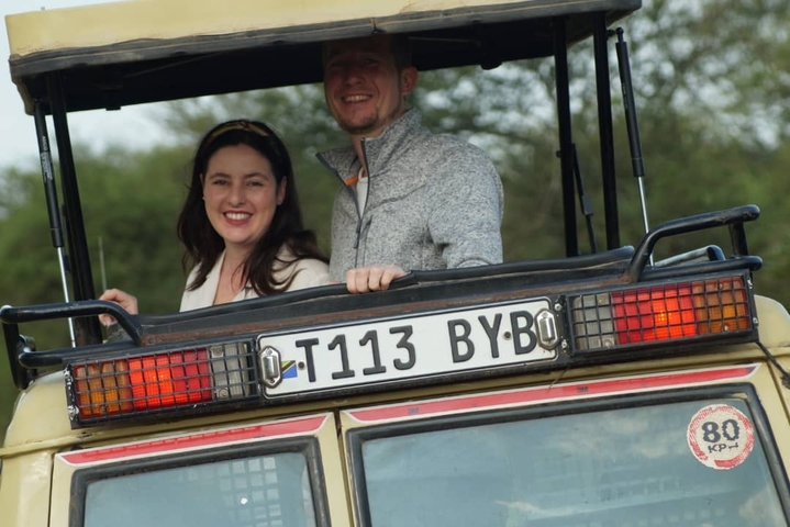       Two people smiling from a safari vehicle.
  
