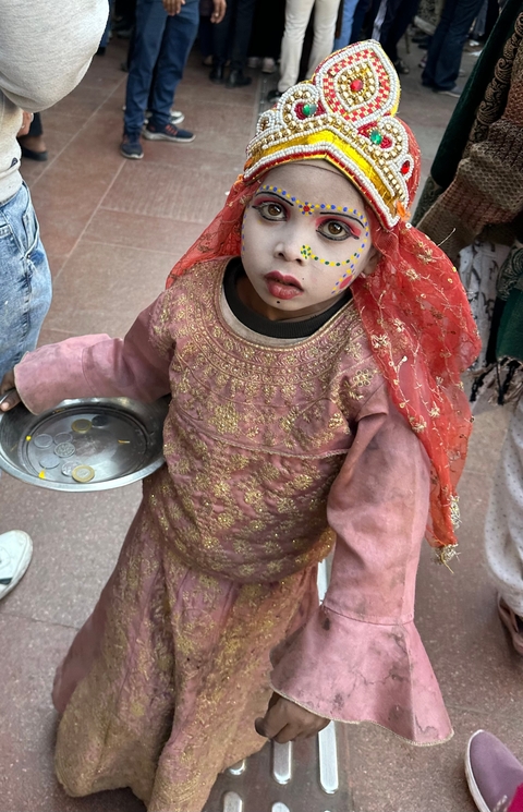       Child in colorful traditional clothing holding coins.
  