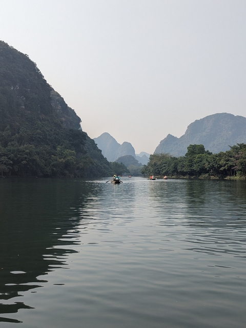       People rowing boats on a river between limestone mountains.
  