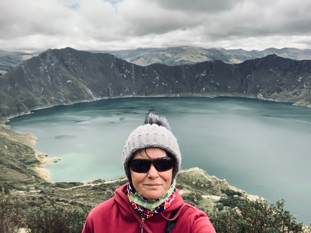 A person in winter clothing with a lake and mountains in the background.
