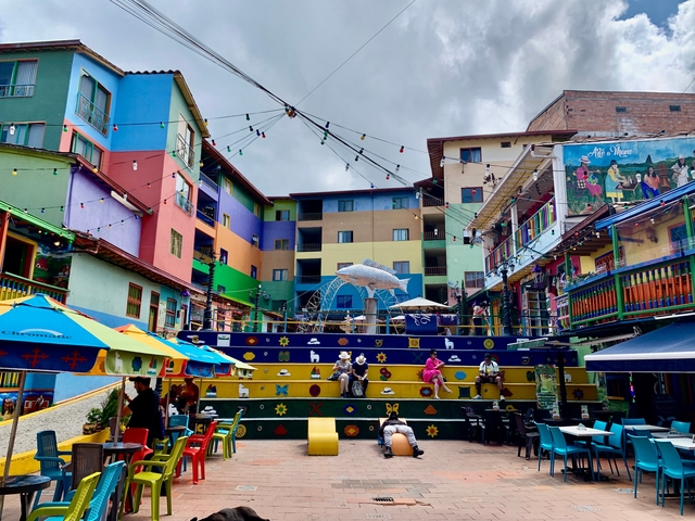 A colorful plaza with people sitting on steps.